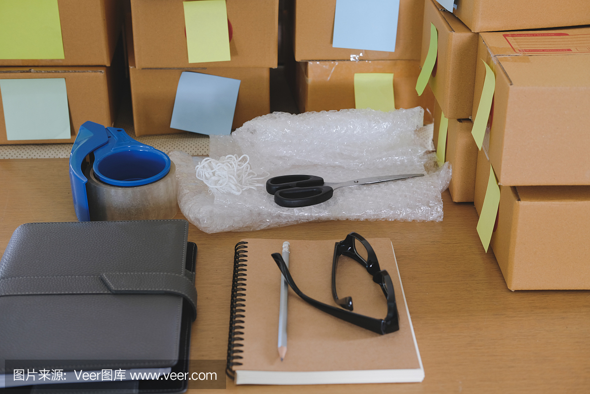 筆記本,小企業(yè)主工作場(chǎng)所的包裝配件。用于網(wǎng)上銷(xiāo)售的紙板箱。企業(yè)家賣(mài)方的書(shū)桌上。電子商務(wù)、運(yùn)輸概念